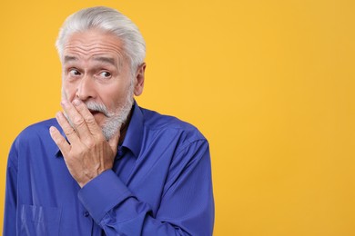 Embarrassed senior man on orange background. Space for text
