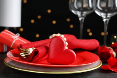 Photo of Beautiful place setting for romantic dinner on table against black background with blurred lights, closeup. Valentine's day celebration