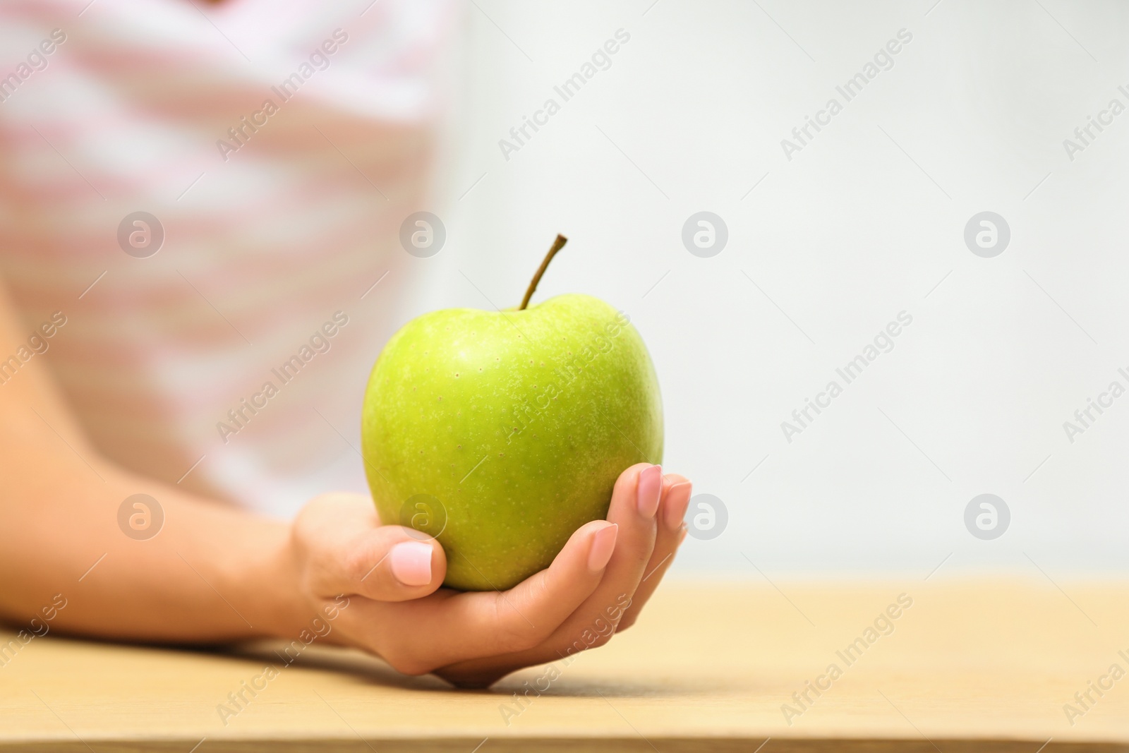Photo of Woman holding fresh green apple at table, closeup. Space for text