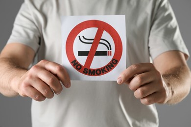 Man holding card with no smoking sign on gray background, closeup