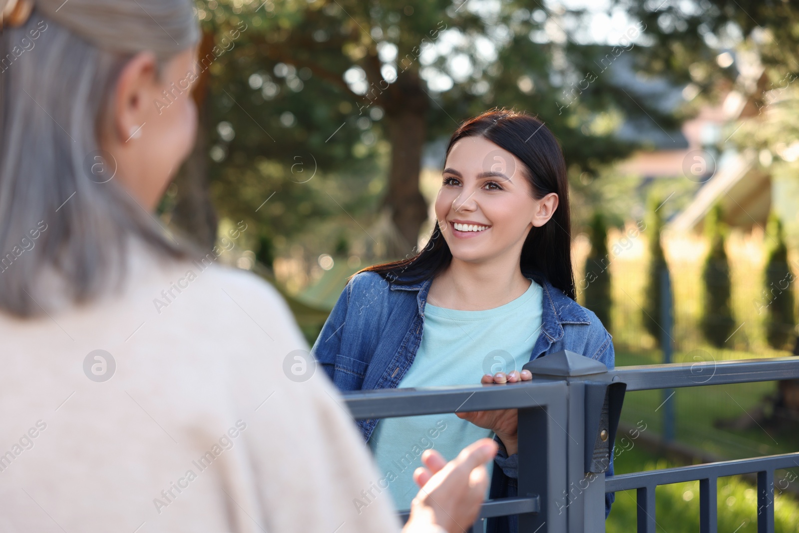 Photo of Friendly relationship with neighbours. Happy women near fence outdoors