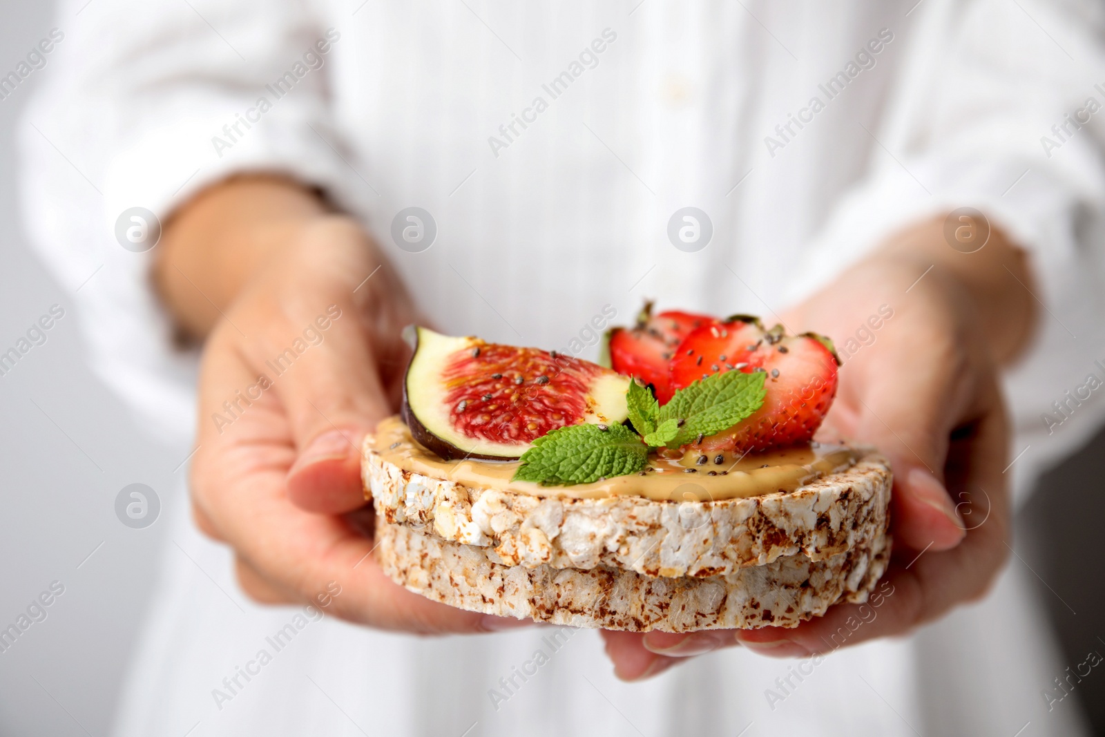 Photo of Woman holding tasty crispbreads with peanut butter, strawberries, mint and fig, closeup