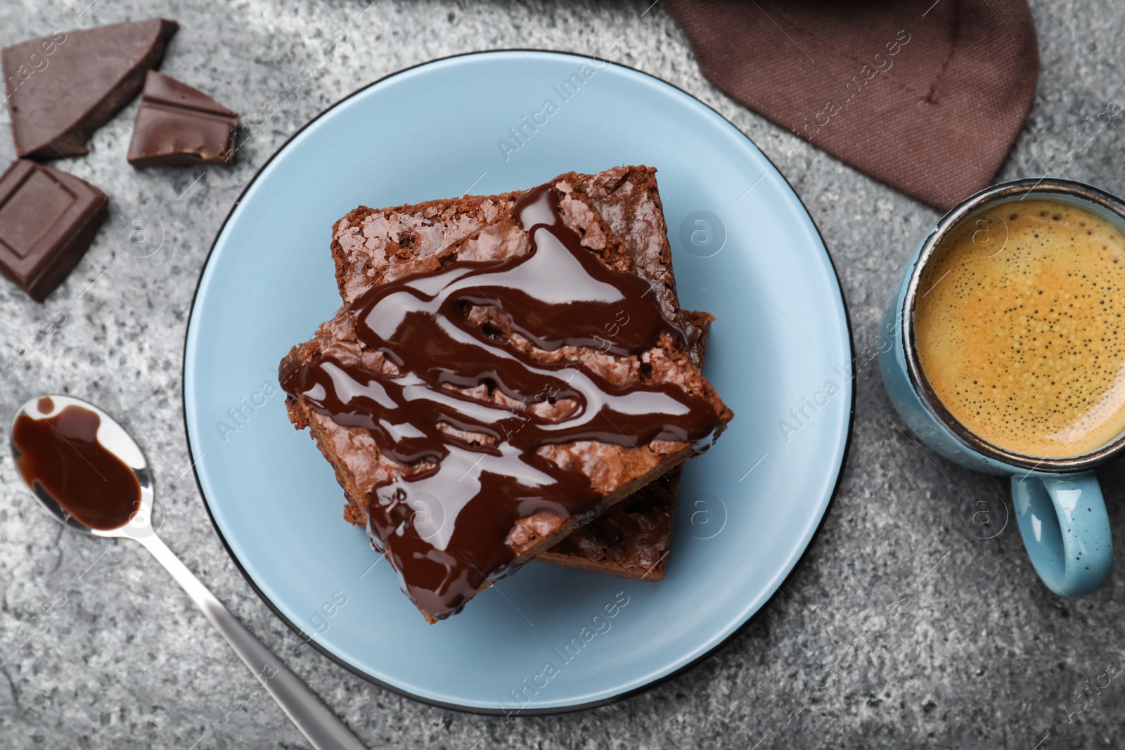 Photo of Delicious chocolate brownies with sweet syrup served on grey table, flat lay