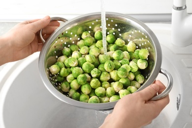 Photo of Woman washing fresh Brussels sprouts in colander, closeup