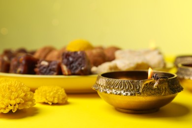 Photo of Happy Diwali. Diya lamp, chrysanthemum flowers and delicious Indian sweets on yellow table, closeup