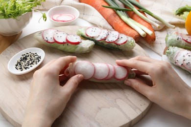 Photo of Woman wrapping spring roll at table with products, closeup