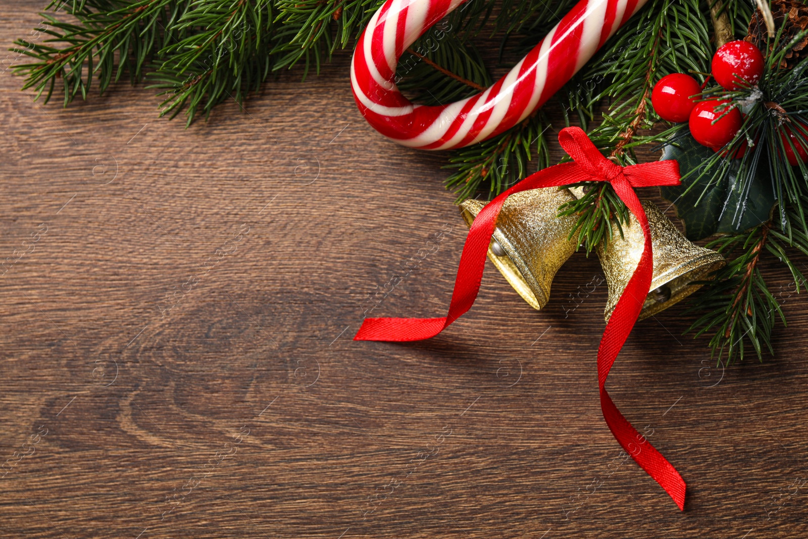 Photo of Christmas bells and fir tree branches with festive decor on wooden table, flat lay. Space for text