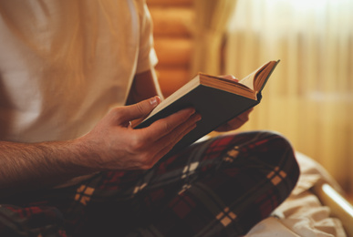 Young man reading book on bed at home, closeup