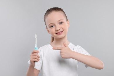 Photo of Happy girl holding electric toothbrush on light grey background