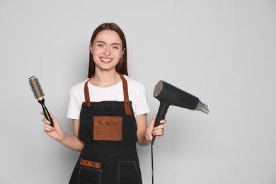 Photo of Portrait of happy hairdresser with hairdryer and brush on light background. Space for text