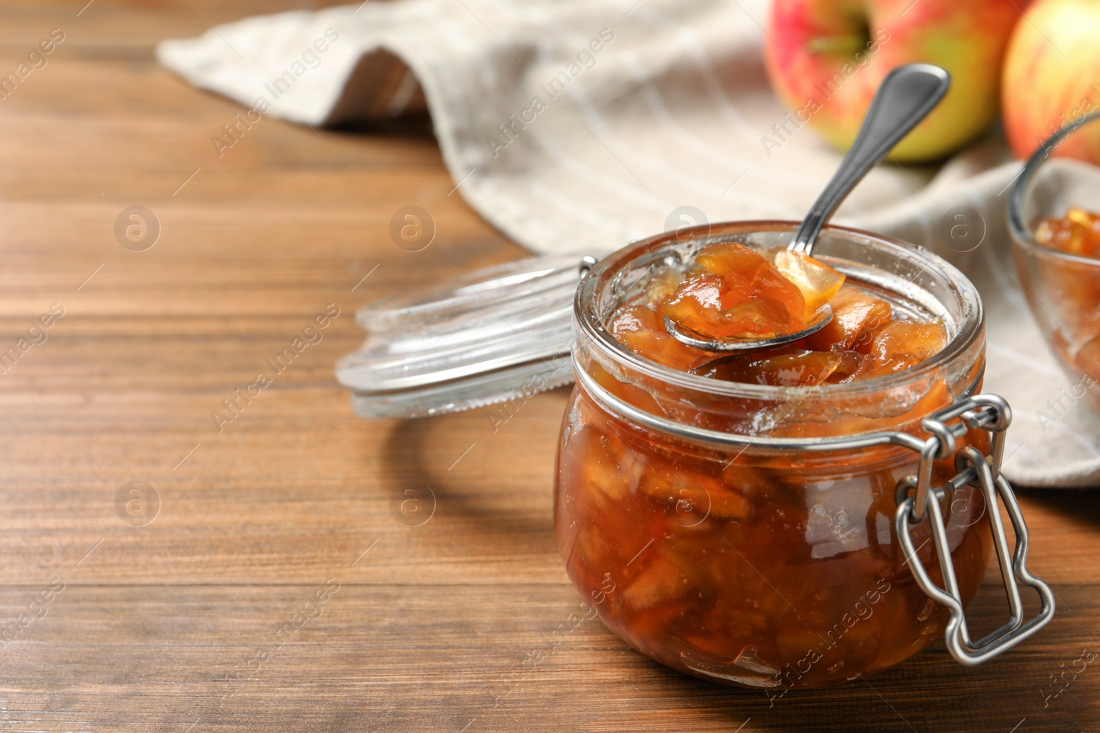 Photo of Tasty apple jam and spoon in glass jar on wooden table, closeup. Space for text