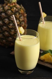 Photo of Tasty pineapple smoothie and fruit on black table