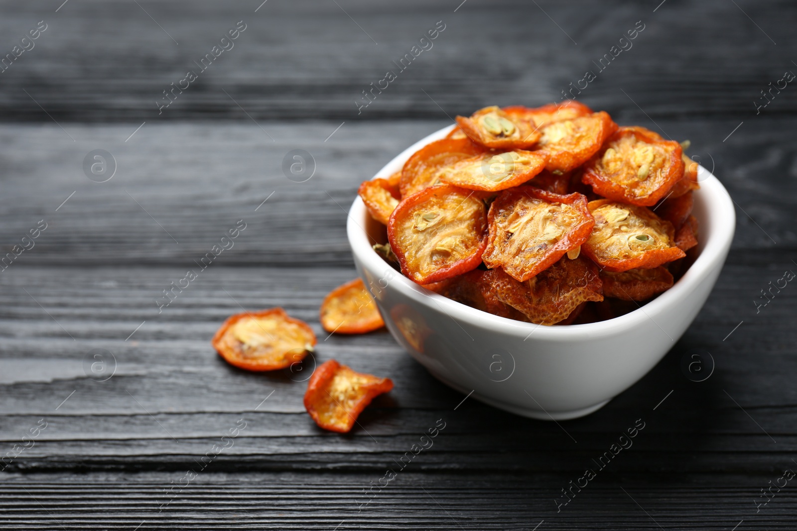 Photo of Bowl with cut dried kumquat fruits on black wooden table, closeup. Space for text