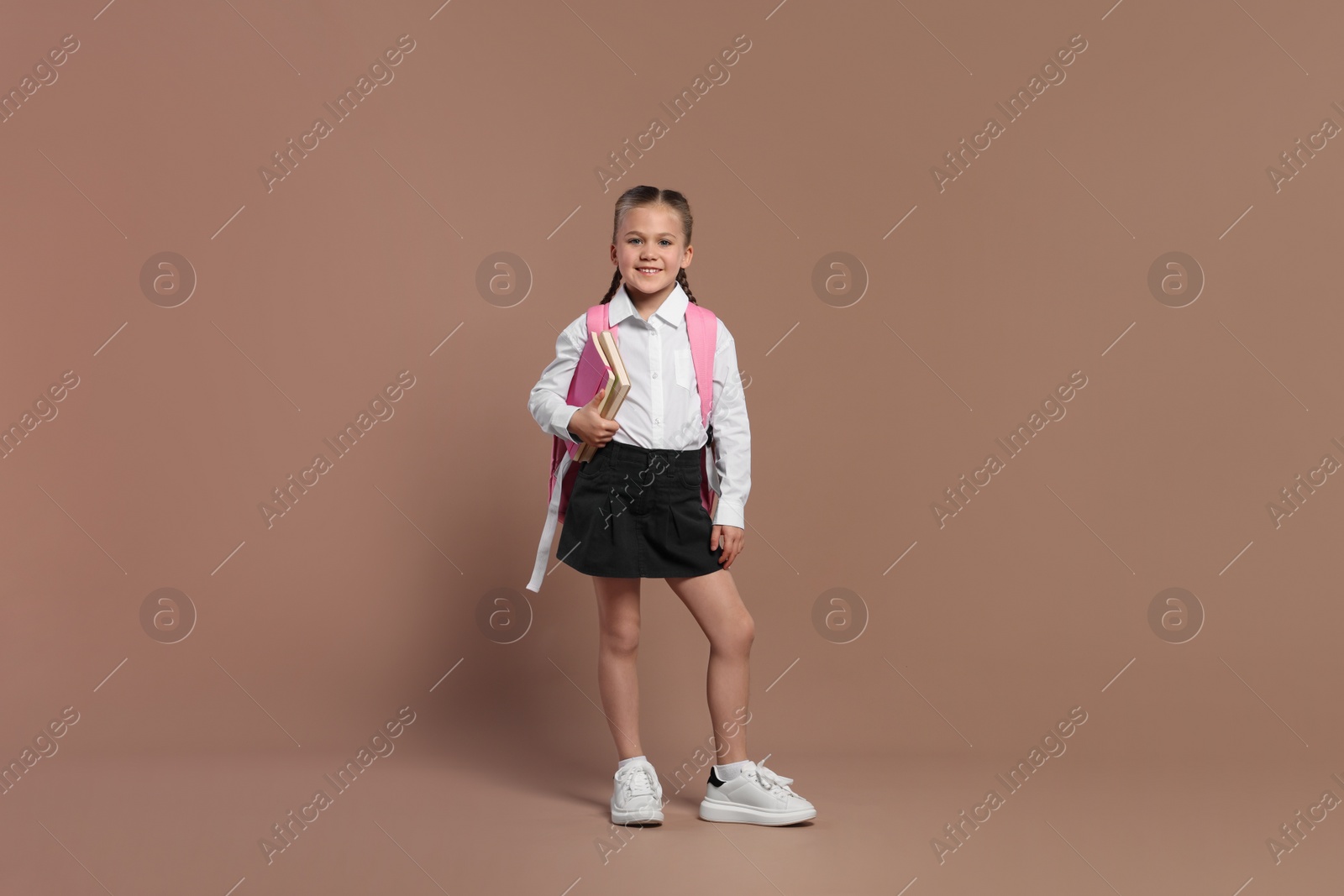 Photo of Happy schoolgirl with backpack and books on brown background