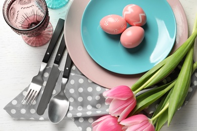 Photo of Festive Easter table setting with painted eggs on wooden background, top view