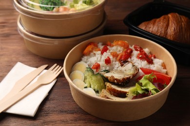 Tasty food in containers with knife and fork on wooden table, closeup