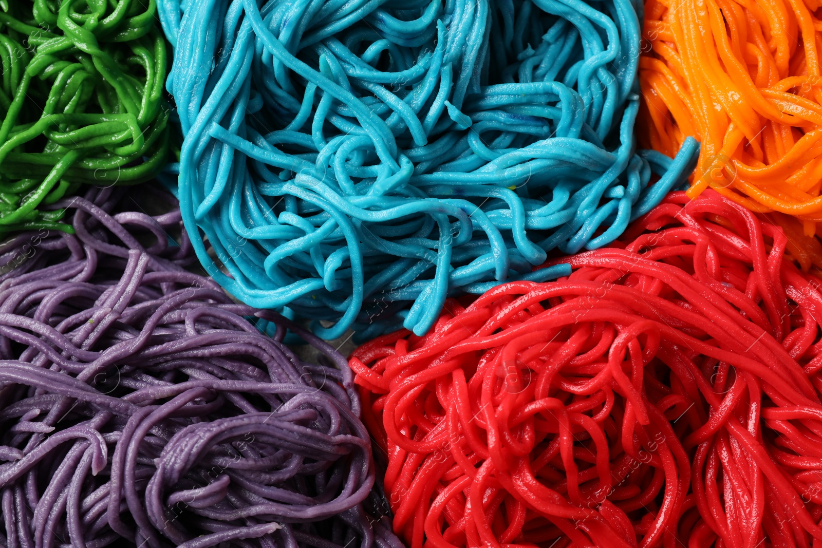 Photo of Rolled spaghetti painted with different food colorings as background, closeup