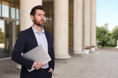 Successful lawyer with laptop near building outdoors, space for text