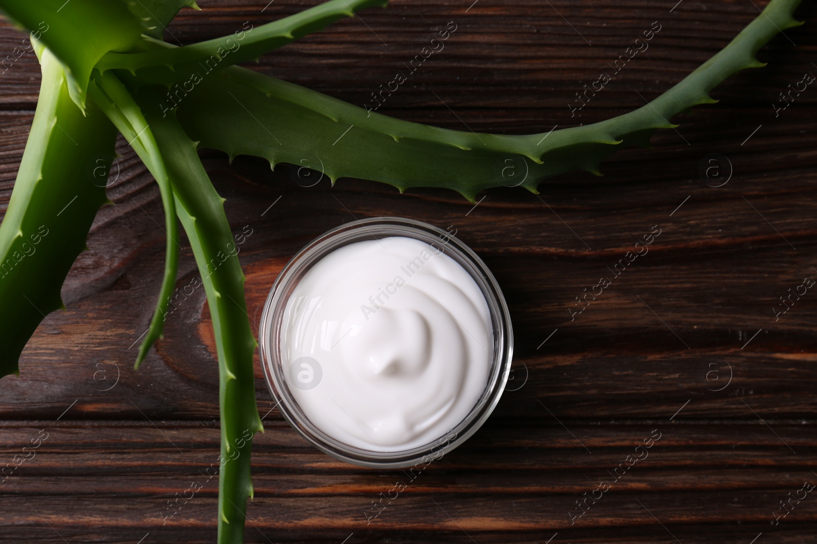 Photo of Bowl of cosmetic cream and aloe vera leaves on wooden table, flat lay
