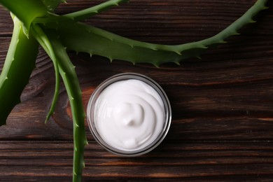 Bowl of cosmetic cream and aloe vera leaves on wooden table, flat lay