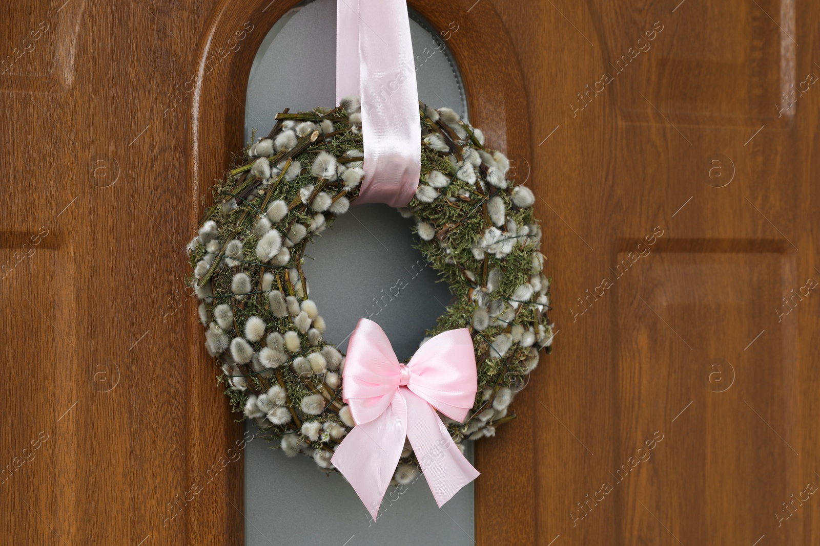 Photo of Wreath made of beautiful willow branches and pink bow on wooden door