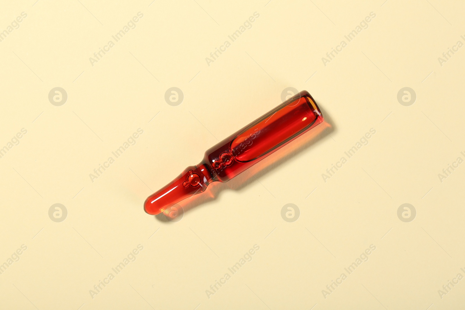 Photo of Glass ampoule with liquid on beige background, top view