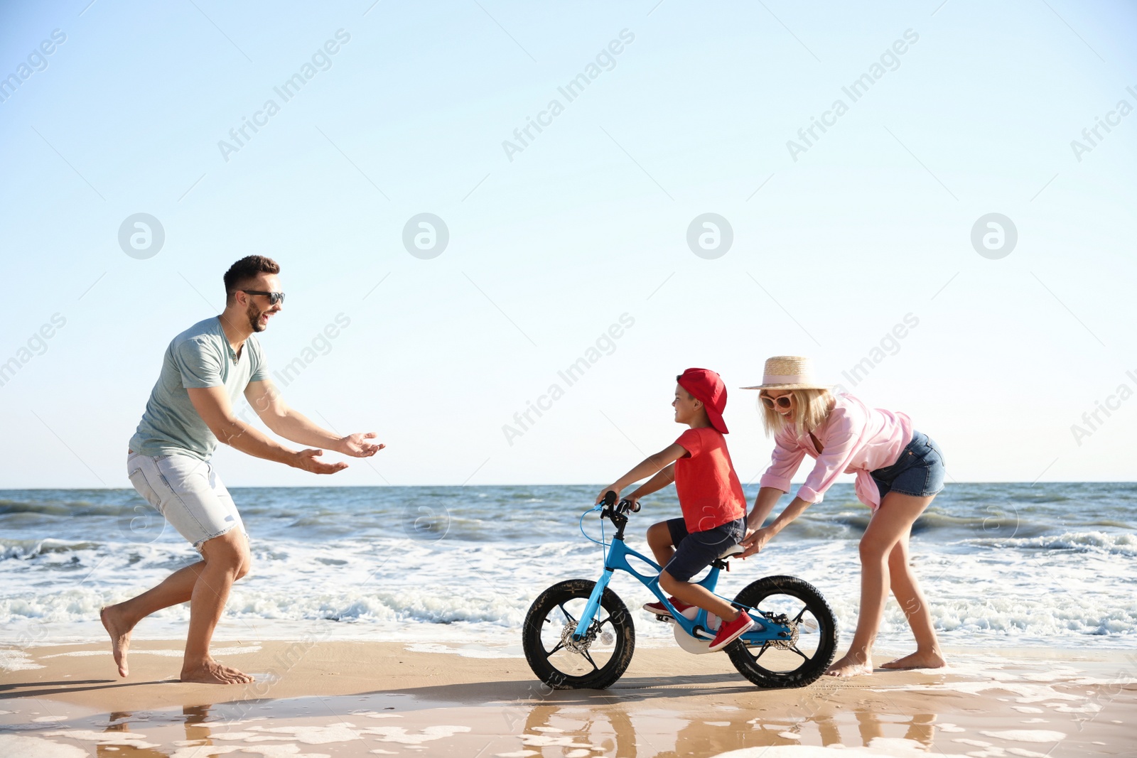 Photo of Happy parents teaching son to ride bicycle on sandy beach near sea