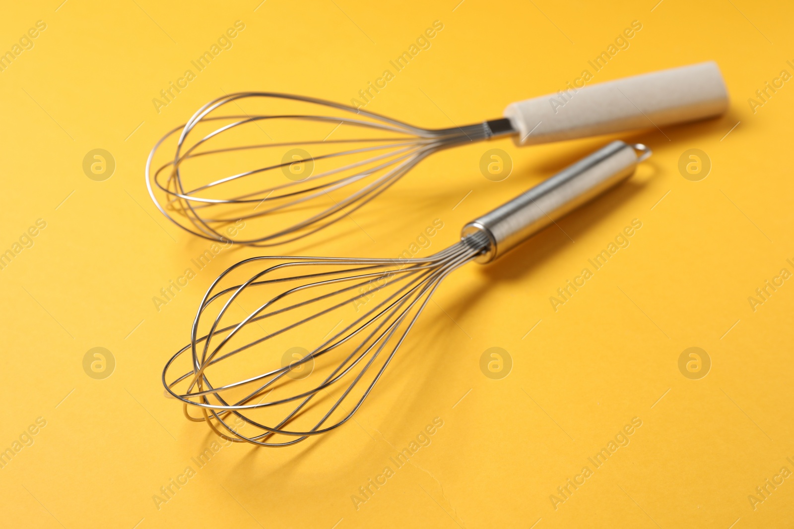 Photo of Two metal whisks on yellow background, closeup. Kitchen tool