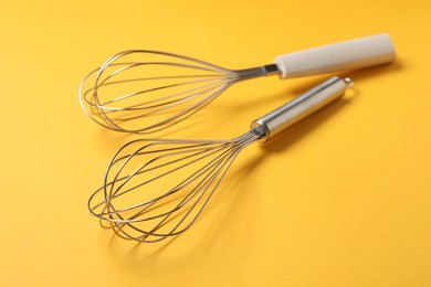 Two metal whisks on yellow background, closeup. Kitchen tool