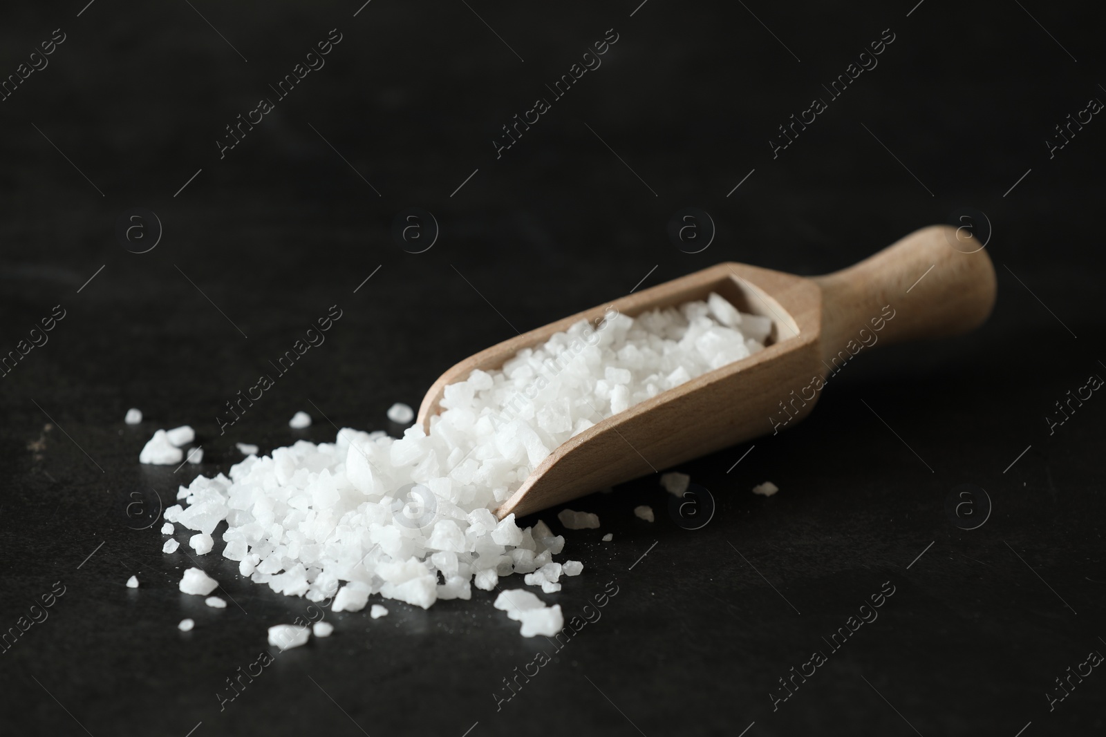 Photo of Organic salt and wooden scoop on black table