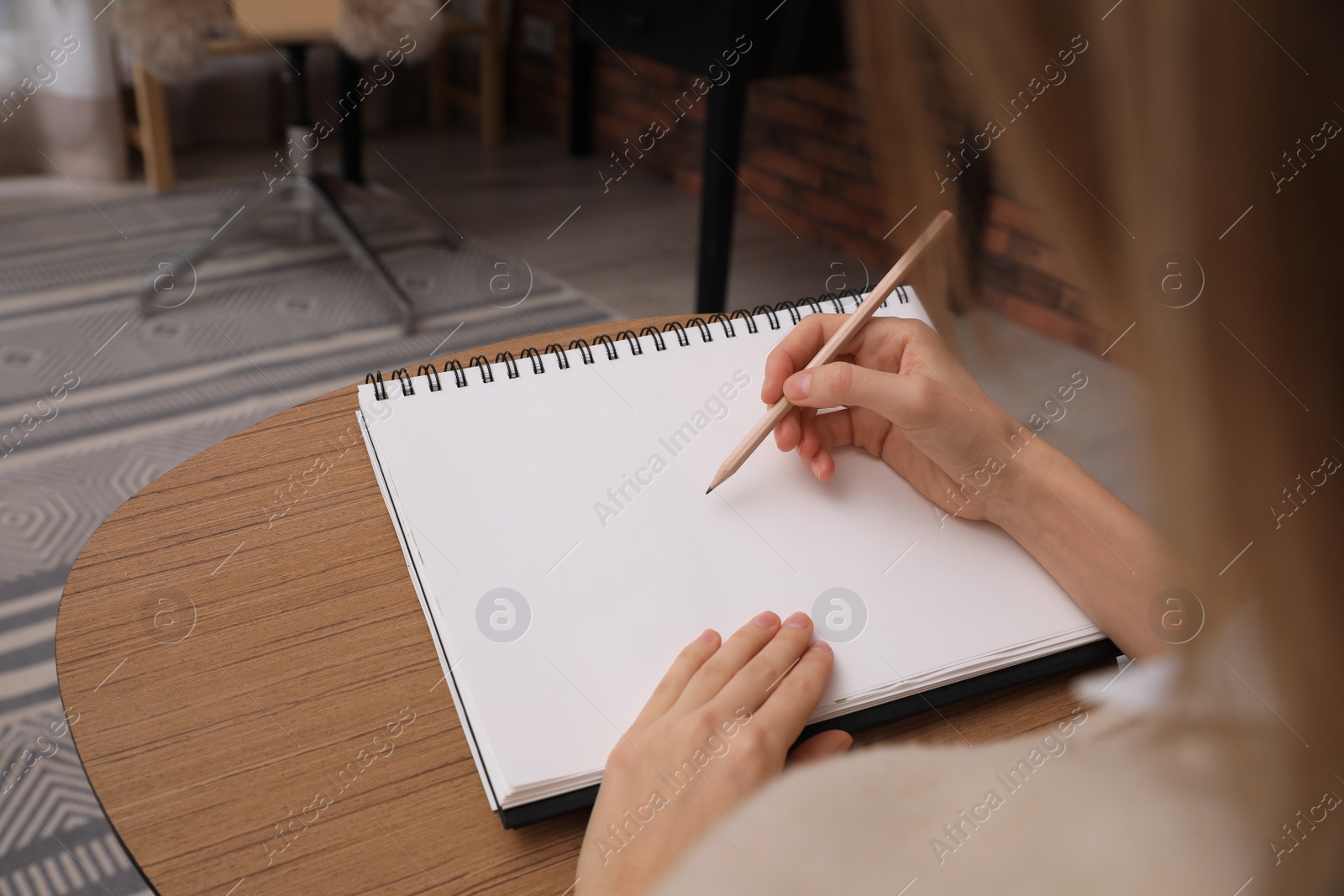 Photo of Woman drawing in sketchbook with pencil at home, closeup