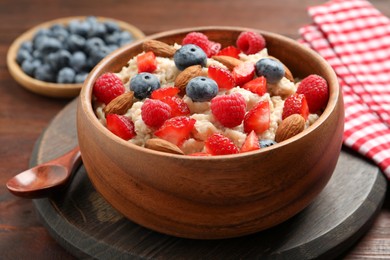 Photo of Tasty oatmeal porridge with berries and almond nuts in bowl served on wooden table