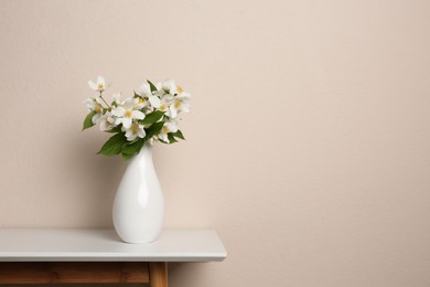 Photo of Bouquet of beautiful jasmine flowers in vase on table near beige wall, space for text