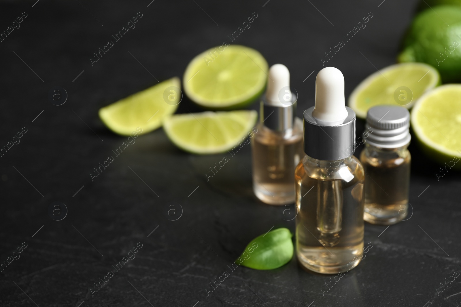 Photo of Lime essential oil and cut citrus fruits on black table. Space for text