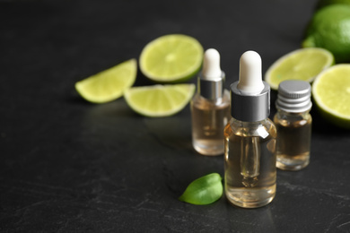 Lime essential oil and cut citrus fruits on black table. Space for text