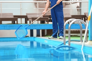 Photo of Male worker cleaning outdoor pool with scoop net