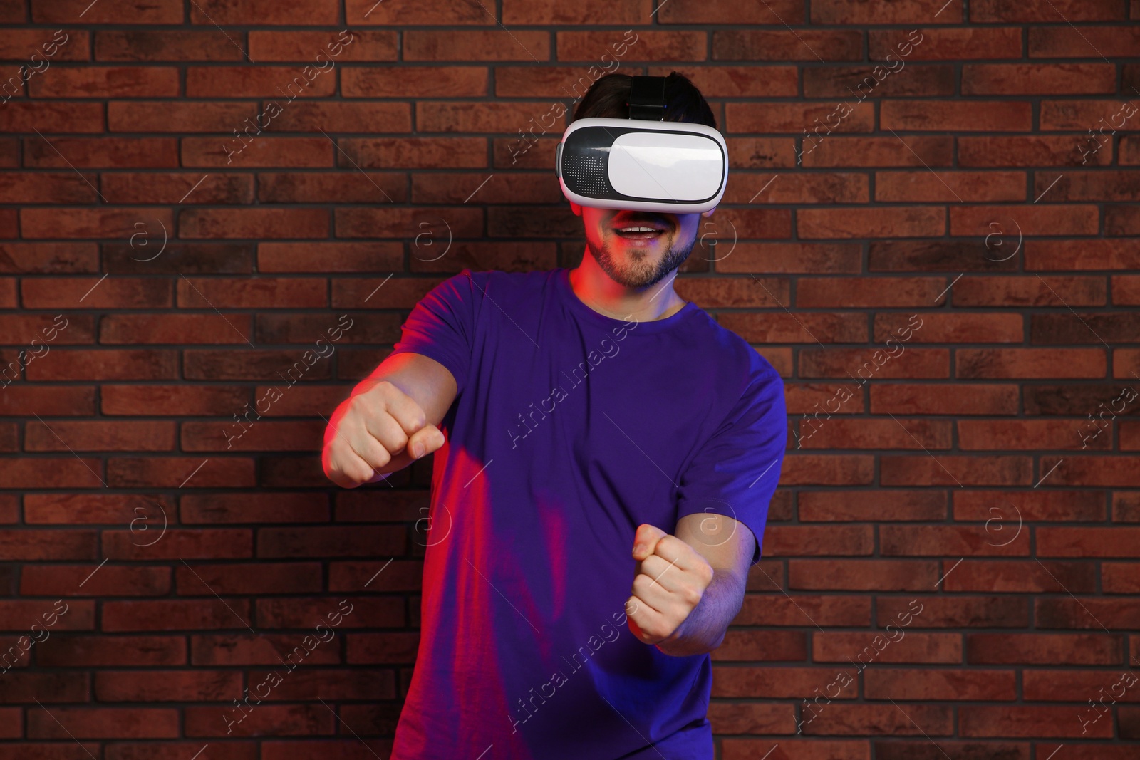 Photo of Emotional man playing video games with virtual reality headset near brick wall