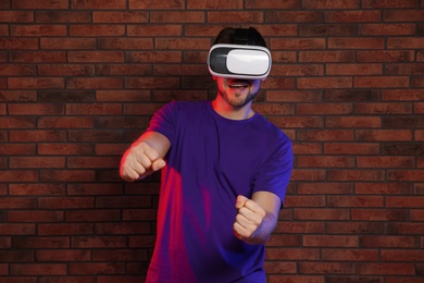 Emotional man playing video games with virtual reality headset near brick wall