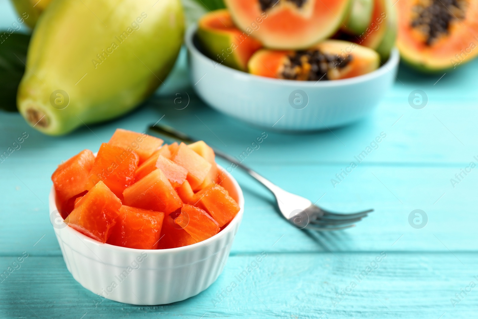 Photo of Dices of fresh ripe papaya in bowl on turquoise wooden table