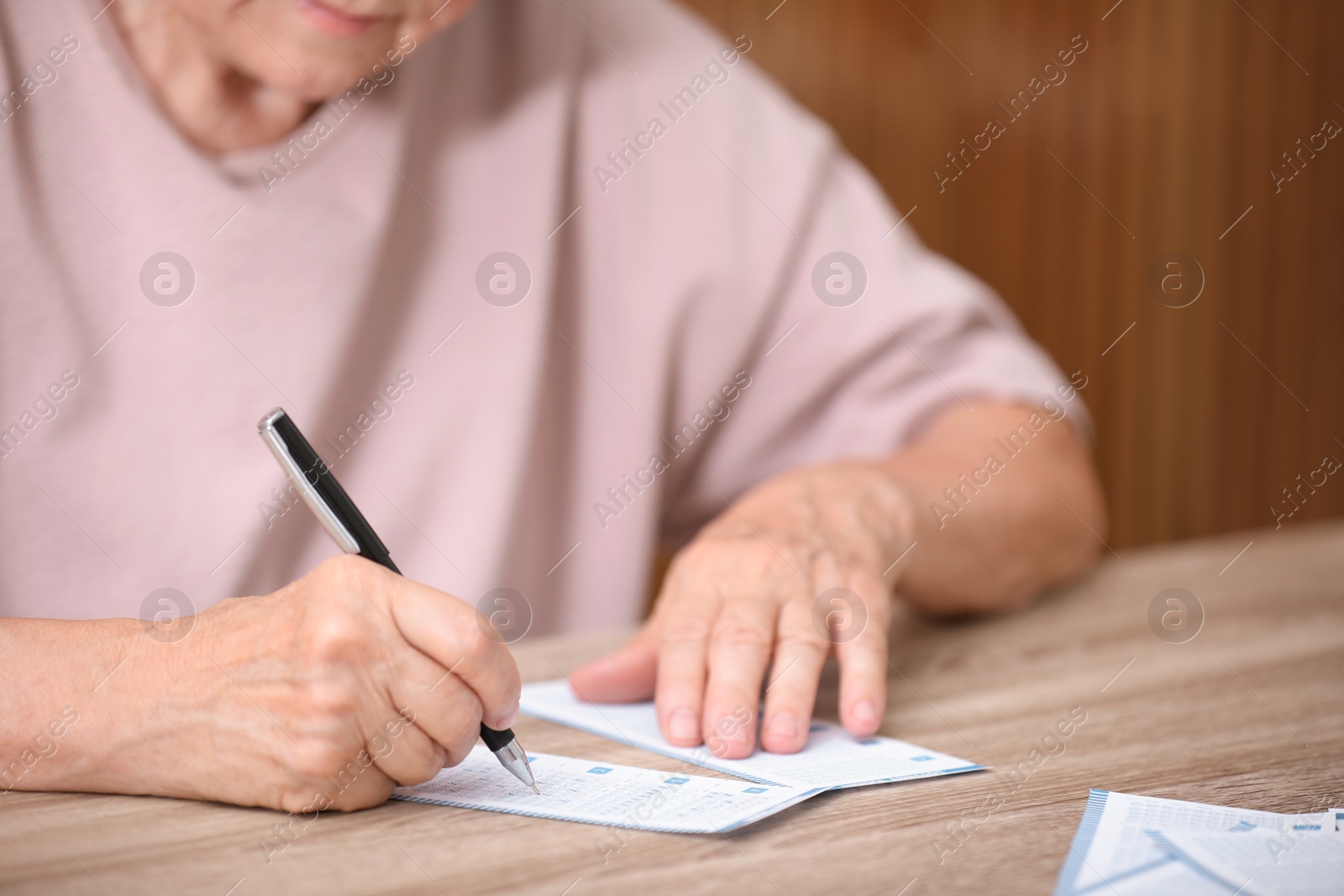 Photo of Senior woman filling out lottery ticket at table, closeup