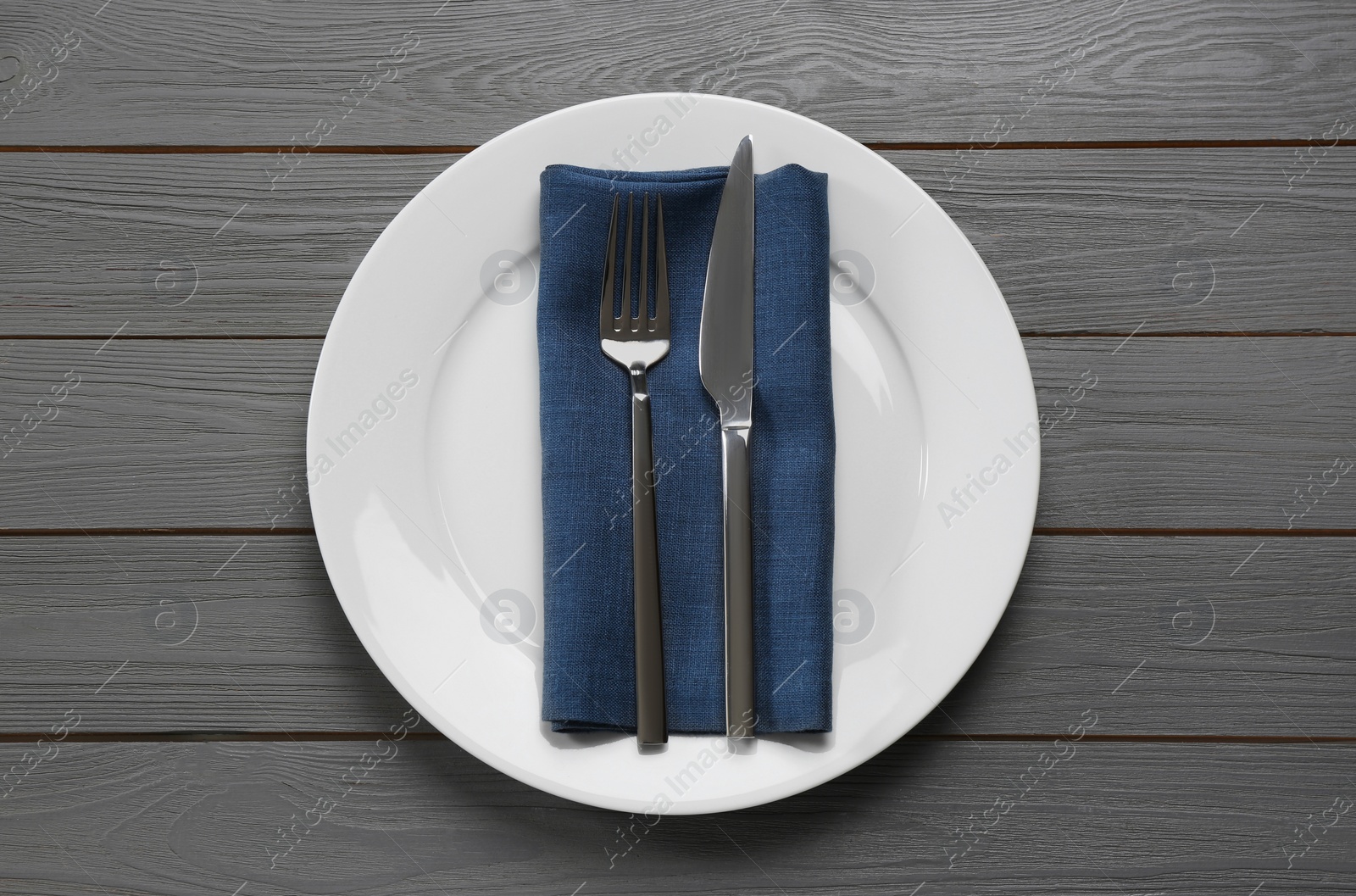 Photo of Clean plate with shiny silver cutlery on grey wooden table, flat lay