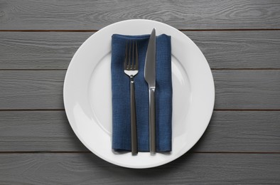 Photo of Clean plate with shiny silver cutlery on grey wooden table, flat lay