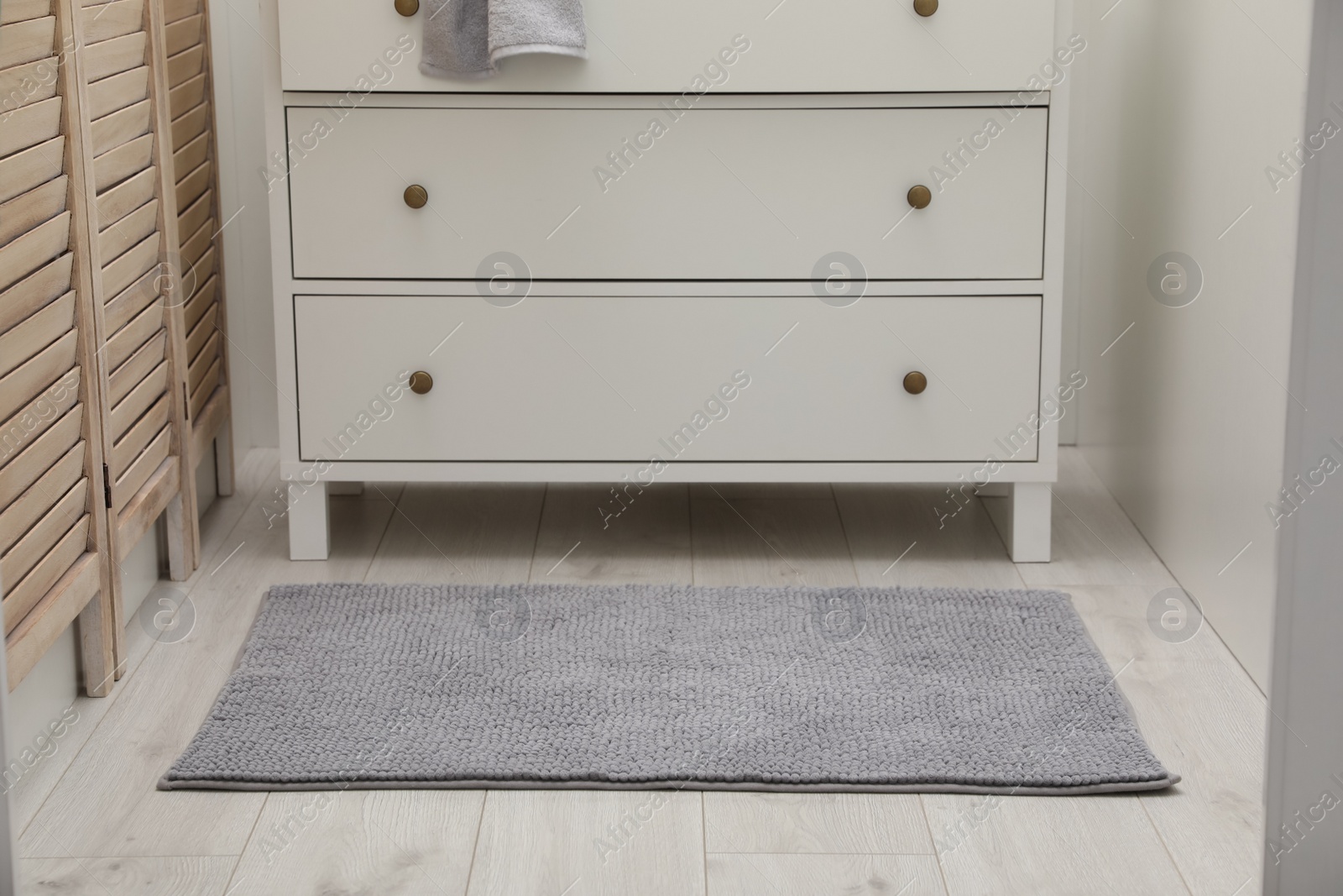 Photo of Grey bath mat near chest of drawers indoors