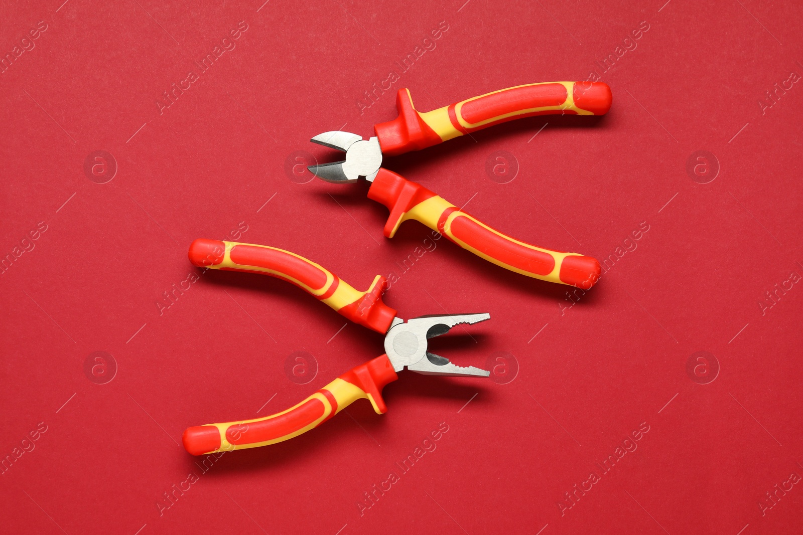 Photo of Two pliers on red background, flat lay