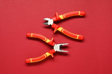 Photo of Two pliers on red background, flat lay