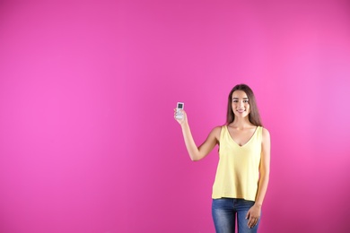 Young woman switching on air conditioner on color background