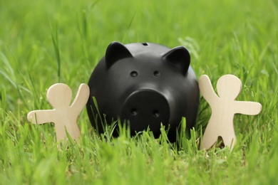 Photo of Cute piggy bank and wooden people on green grass in park