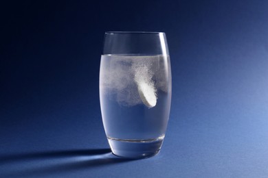Photo of Effervescent pill dissolving in glass of water on blue background