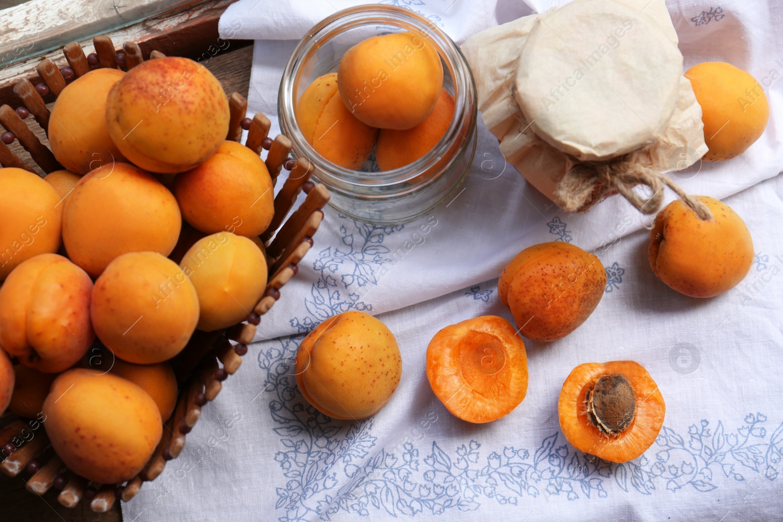 Photo of Jars and fresh ripe apricots on white tablecloth. Fruit preserve