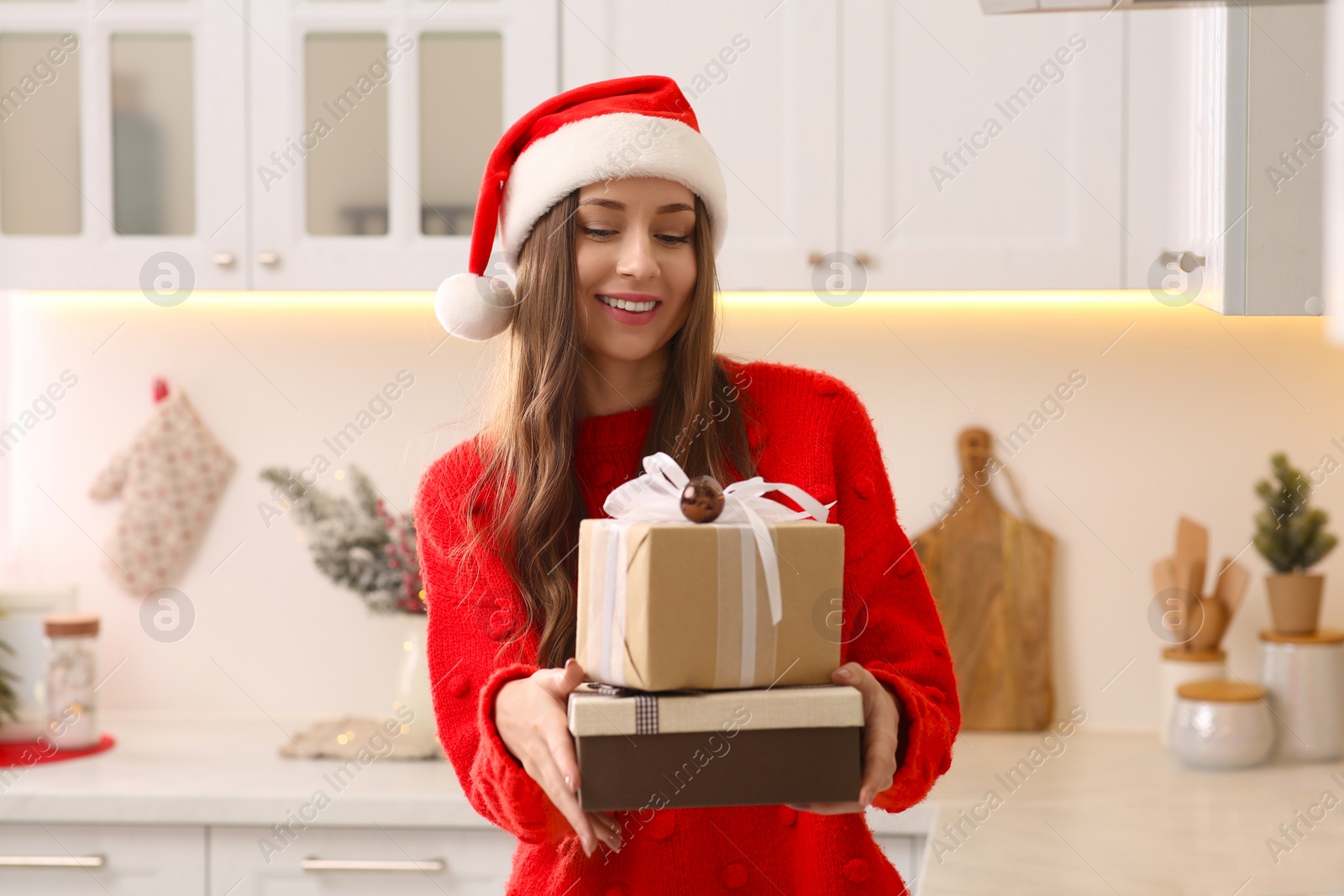 Photo of Beautiful young woman in Santa hat with presents in kitchen. Celebrating Christmas